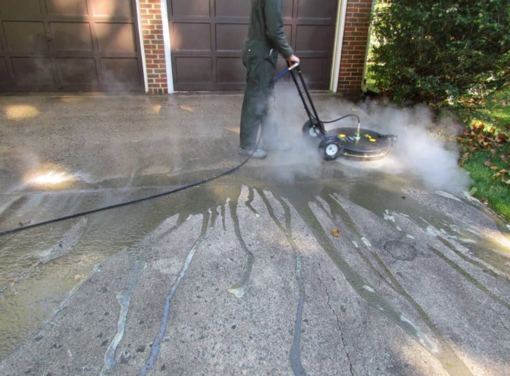 Technician using a walk-behind surface cleaner on a residential concrete driveway