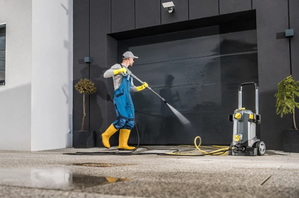 Worker in safety gear pressure washing a large commercial garage door